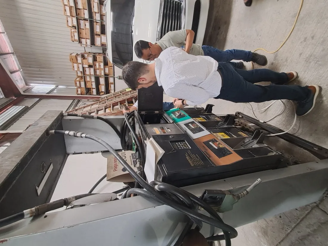 Dos técnicos de Master Services trabajando en el dispensador de una estación con mangueras, paneles de control y un vehículo